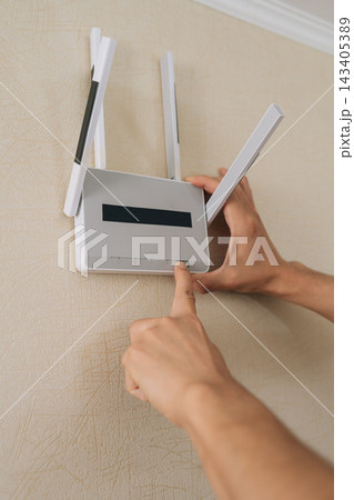 Person hands activating wall mounted wireless router to establish home network connection, ensuring strong internet signal and smart home connectivity. Person hands activating wall mounted wireless router to establish home network connection, ensuring strong internet signal and smart home connectivity. 143405389
