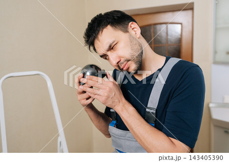 Portrait of male worker in uniform examining black surveillance camera. Close-up portrait of handyman installing home security system. Concept of safety, technology, professional service. Portrait of male worker in uniform examining black surveillance camera. Close-up portrait of handyman installing home security system. Concept of safety, technology, professional service. 143405390