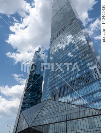 Modern glass skyscrapers with reflective facades rising against a clear blue sky in an urban setting Modern glass skyscrapers with reflective facades rising against a clear blue sky in an urban setting 143405436