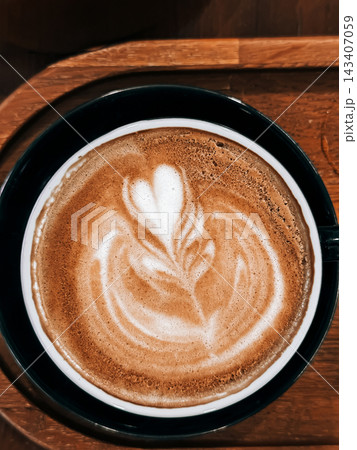 Coffee with heart latte art in a dark ceramic cup on a wooden tray. White foam forms a heart on coffee in a dark cup, with the coffee presented on wooden tray Coffee with heart latte art in a dark ceramic cup on a wooden tray. White foam forms a heart on coffee in a dark cup, with the coffee presented on wooden tray 143407059