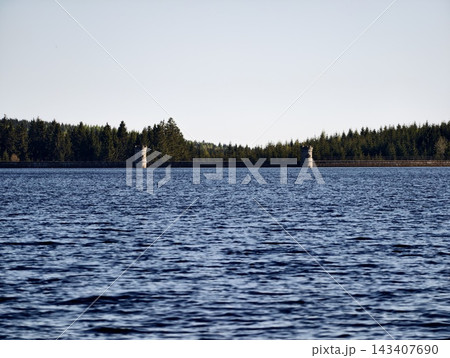 Two signs near tranquil lake. Duo of markers positioned near serene water with pine trees in backdrop Two signs near tranquil lake. Duo of markers positioned near serene water with pine trees in backdrop 143407690