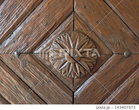 Rectangular wooden door panel featuring carved geometric triangles and riveted studs in weathered brown wood with diamond centerpiece, intricate bevels, aged texture, rustic architectural detail Rectangular wooden door panel featuring carved geometric triangles and riveted studs in weathered brown wood with diamond centerpiece, intricate bevels, aged texture, rustic architectural detail 143407873