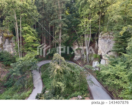 Aerial view of winding forest road weaving through dense canopy amid rocky cliffs and mossy boulders along hillside trail, with forest, road, winding, path detail Aerial view of winding forest road weaving through dense canopy amid rocky cliffs and mossy boulders along hillside trail, with forest, road, winding, path detail 143407876