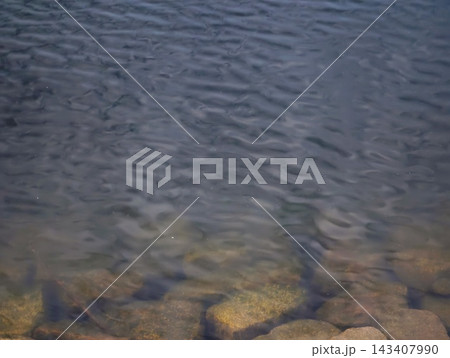 Night ocean water over rocky shoreline with visible submerged stones, faint blue glow, and gentle surf under moonlight Night ocean water over rocky shoreline with visible submerged stones, faint blue glow, and gentle surf under moonlight 143407990