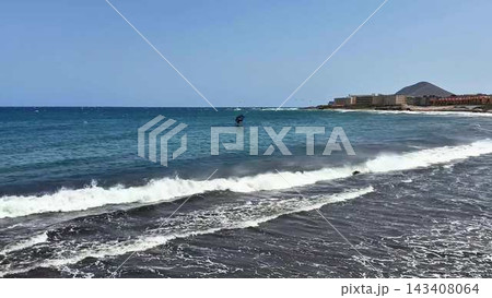 A stunning coastal scene features a kite surfer gliding over the clear blue waters of the ocean A stunning coastal scene features a kite surfer gliding over the clear blue waters of the ocean 143408064
