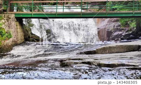 A Serene Waterfall Cascading Gently Under a Charming Bridge amidst Natural Surroundings A Serene Waterfall Cascading Gently Under a Charming Bridge amidst Natural Surroundings 143408305
