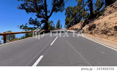 A scenic and beautiful mountain road, surrounded by lush green pines under clear blue skies 143408358