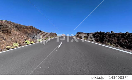 A picturesque scenic road winding through a volcanic lava landscape beneath a clear blue sky 143408374