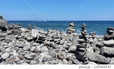 A tranquil shoreline adorned with beautiful stone cairns sitting under clear blue skies 143408541