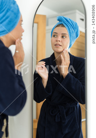 Young woman looking into mirror in bedroom Young woman looking into mirror in bedroom 143408906