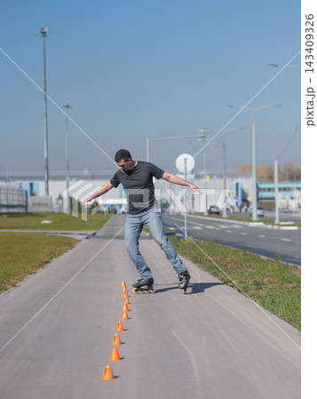 A Caucasian man rollerblades around the slalom course. A Caucasian man rollerblades around the slalom course. 143409326
