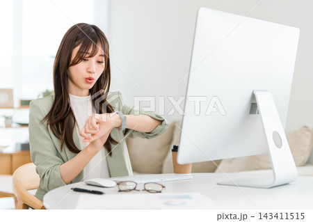 仕事中に腕時計で時間を確認する女性。忙しいビジネスと時間管理 仕事中に腕時計で時間を確認する女性。忙しいビジネスと時間管理 143411515