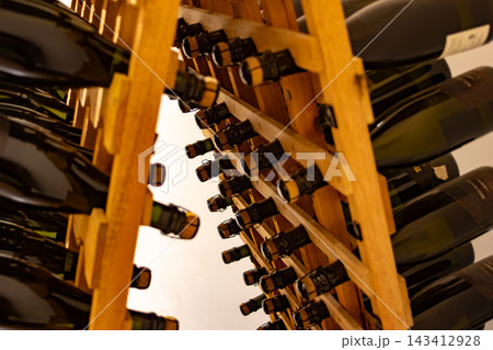 Sparkling wine bottles aging in wooden riddling racks, undergoing the traditional method of fermentation in a cellar, developing complex flavors for future enjoyment 143412928