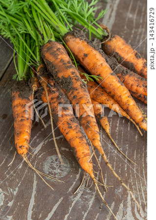 Freshly harvested carrots with dirt on wooden table showcasing vibrant orange colors and leafy tops perfect for healthy meals and snacks 143416729