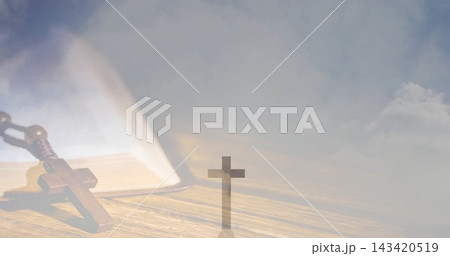 Resting wooden rosary and open book lying on wooden tabletop, with small upright cross silhouette 143420519