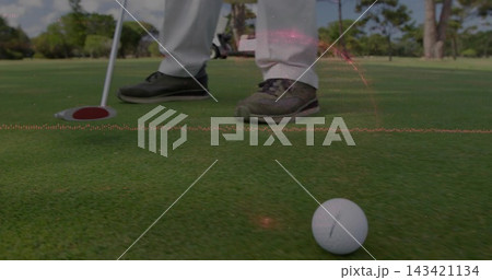 Lining up golfer in light-trousers dark-golf-shoes on green, with golf ball, putter, red-rim cup Lining up golfer in light-trousers dark-golf-shoes on green, with golf ball, putter, red-rim cup 143421134