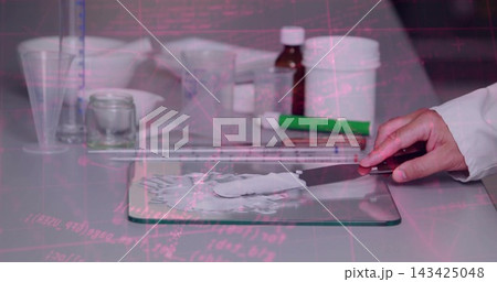 Spreading ointment on glass slab, right hand in lab coat holding spatula at pharmacy workstation 143425048