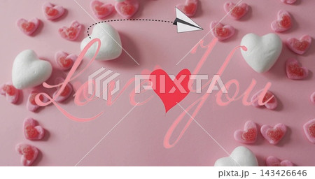 Showing Valentine display on pink table marshmallows pink gummy hearts cursive Love You paper plane 143426646