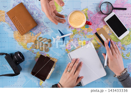 Two people are discussing travel plans at a table with a map, coins, a camera, coffee, and notebooks. They are preparing for an upcoming journey while enjoying their drinks. Two people are discussing travel plans at a table with a map, coins, a camera, coffee, and notebooks. They are preparing for an upcoming journey while enjoying their drinks. 143433336