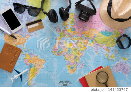 Various travel items are spread out on a world map. A camera, headphones, and a phone are visible alongside a passport and a toy airplane. These items suggest preparation for a journey. Various travel items are spread out on a world map. A camera, headphones, and a phone are visible alongside a passport and a toy airplane. These items suggest preparation for a journey. 143433747