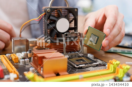 A technician works on a computer motherboard, carefully placing a new CPU into its slot. The workspace includes various components like a fan and heatsink. Tools are nearby for the upgrade. A technician works on a computer motherboard, carefully placing a new CPU into its slot. The workspace includes various components like a fan and heatsink. Tools are nearby for the upgrade. 143434410