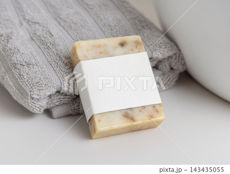Herbal soap with blank label mockup near grey towel in beige bathroom, unbranded packaging Herbal soap with blank label mockup near grey towel in beige bathroom, unbranded packaging 143435055