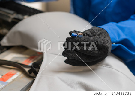 A mechanic is holding a burnt-out fuse and a new one. A mechanic is holding a burnt-out fuse and a new one. 143438733
