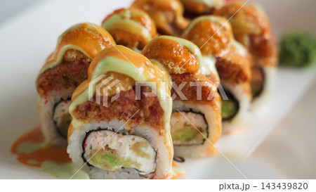 Sushi rolls presenting vibrant orange and green sauces, filled with spicy tuna, crab meat, avocado, and cream cheese 143439820