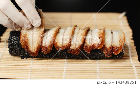 Chef preparing unagi sushi, arranging grilled eel slices on a roll of black rice, making traditional Japanese food Chef preparing unagi sushi, arranging grilled eel slices on a roll of black rice, making traditional Japanese food 143439851