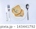 Moldy bread on a white plate next to silverware in a simple setting during daytime 143441792