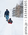 Child rides sled while adult pulls it through snow in city during winter afternoon 143441805