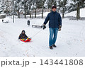 Father pulls child on sled in snowy park during winter afternoon 143441808