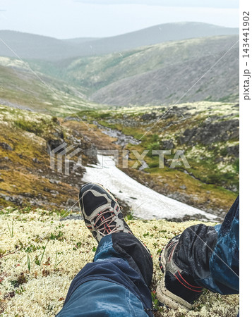 Hiker's legs in trekking shoes resting on mountain slope Hiker's legs in trekking shoes resting on mountain slope 143441902