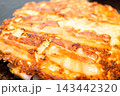 鉄板の上で香ばしく焼き上げられたミックス豚玉、豚肉が乗ったお好み焼き 143442320
