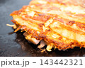 鉄板の上で香ばしく焼き上げられたミックス豚玉、豚肉が乗ったお好み焼き 143442321