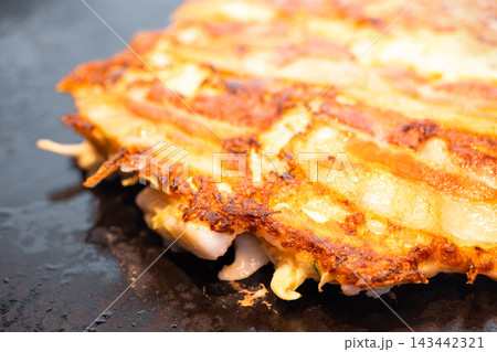 鉄板の上で香ばしく焼き上げられたミックス豚玉、豚肉が乗ったお好み焼き 143442321