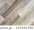 Diagonal wood floor planks texture with natural grain patterns. Modern laminate flooring in neutral beige, grey, and brown tones for interior design background. Close-up of rustic timber surface. 143442380