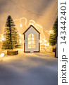 Miniature wooden toy house with Christmas trees and glowing lights. 143442401