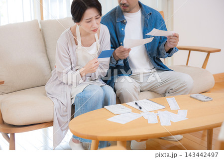 通帳を見ながら住宅ローンの金利上昇や物価高で家計に悩む日本人夫婦、返済負担、生活費、家計ひっ迫顔無し 通帳を見ながら住宅ローンの金利上昇や物価高で家計に悩む日本人夫婦、返済負担、生活費、家計ひっ迫顔無し 143442497