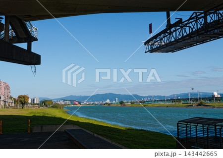 Riverside park view from beneath a bridge toward distant mountains and city Riverside park view from beneath a bridge toward distant mountains and city 143442665