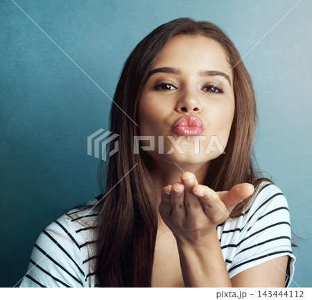 Blowing kiss, blue background and portrait of woman for romance, affection and gratitude in studio. Beauty, confidence and face of person with flirting emoji, positive hand gesture and thank you 143444112