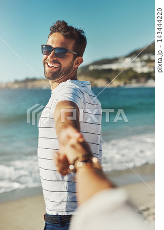 Happy couple, smile and holding hands with partner by ocean with sunglasses for travel vacation with happiness. Man, summer and pov for walking on beach for holiday, love and trust in Cape Town 143444220