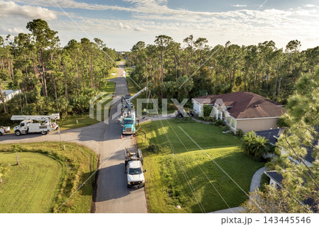 Electrician workers repairing damaged power lines using bucket trucks after hurricane in Florida residential area 143445546