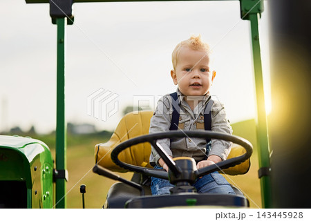 Portrait, child and play on tractor on farm outdoor in countryside for learning agriculture in nature. Boy kid, farmer and drive steering wheel for growth or development of toddler in summer sunshine 143445928