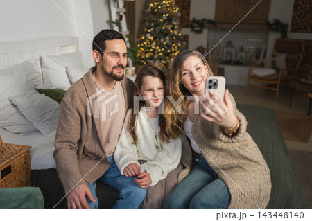Merry Christmas celebrating. Happy family mother father girl child having video chat in smartphone. Parents kid recording video in social network. Family having video call with friends family 143448140