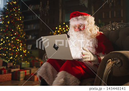 Merry Christmas. Santa Claus with laptop reading letters from children typing buying presents gifts online. Santa with computer on Christmas eve. Mail gifts of Santa Claus. Winter Holiday Celebrations Merry Christmas. Santa Claus with laptop reading letters from children typing buying presents gifts online. Santa with computer on Christmas eve. Mail gifts of Santa Claus. Winter Holiday Celebrations 143448141