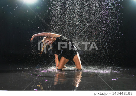 Contemporary woman dancer posing in rain water on black background. Female artist performer dancing with expression. Modern ballerina dancing in darkness. Passion dance in dark. Flexibility balance Contemporary woman dancer posing in rain water on black background. Female artist performer dancing with expression. Modern ballerina dancing in darkness. Passion dance in dark. Flexibility balance 143448195