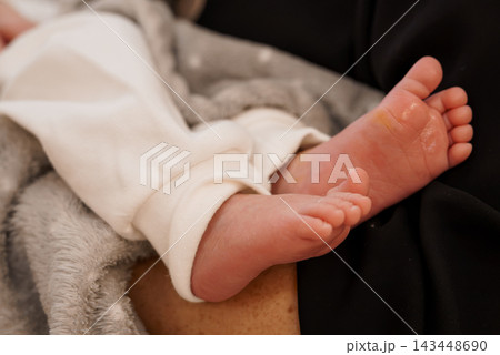 Closeup of infant feet in white sleepwear resting on soft grey blanket with peeling newborn skin texture Closeup of infant feet in white sleepwear resting on soft grey blanket with peeling newborn skin texture 143448690