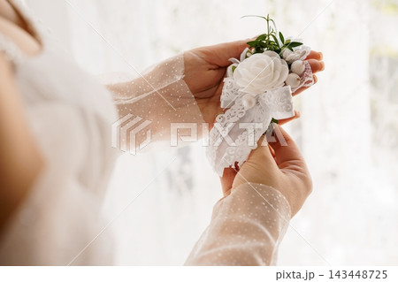 Bride handing white lace rose wedding bouquet to assistant in soft daylight 143448725