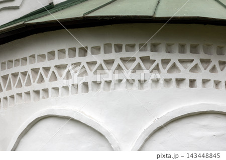 White plaster wall with carved arches and a row of triangular elements under green roof White plaster wall with carved arches and a row of triangular elements under green roof 143448845